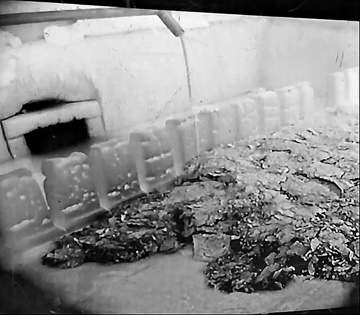 Worn glass-furnace bottom seen from inside, with debris on the paving blocks